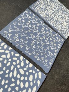 Three pieces of blue paper with white botanical and abstract patterns are arranged diagonally on a dark surface. - Spruced Studio Upscale Workshop