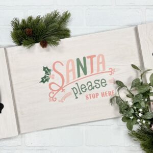 The "11x17 Tray - Santa Please Stop Here" is a white wooden tray with black handles, festive greenery, and a pink flower, featuring "Santa please stop here" in red and green lettering. - Spruced Studio Upscale Workshop