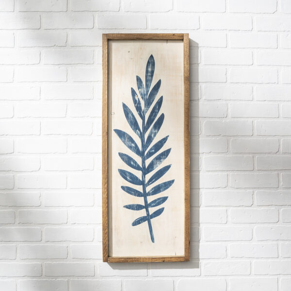 The 12x32 Leaf is a framed artwork showcasing a blue botanical leaf print on a light background, perfect for display on a white brick wall. - Spruced Studio Upscale Workshop