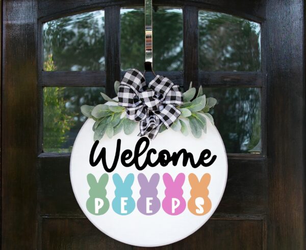 The Welcome Peeps round door sign features a black-and-white checkered bow, green leaves, and the phrase "Welcome Peeps" above pastel bunny silhouettes. - Spruced Studio Upscale Workshop