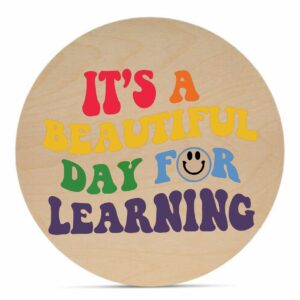 The 18 Round - Beautiful Day for Learning is a wooden circle sign featuring colorful, retro-style text that says "It's a beautiful day for learning" with a smiley face inside the letter "O. - Spruced Studio Upscale Workshop