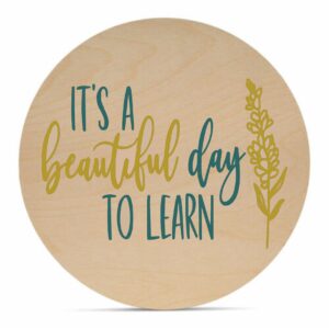 The 18 Round - Beautiful Day to Learn is a wooden circle sign featuring "It's a beautiful day to learn" in blue and gold script and a simple gold botanical illustration. - Spruced Studio Upscale Workshop