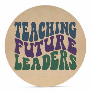 The 18 Round - Teaching Future Leaders is a wooden sign featuring the phrase "Teaching Future Leaders" in bold, retro-style blue, purple, and green lettering. - Spruced Studio Upscale Workshop