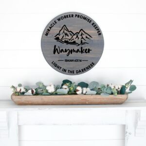 The 18 Round Waymaker wooden sign with mountains and text hangs above a white mantel adorned with greenery and cotton stems in a wooden tray. - Spruced Studio Upscale Workshop