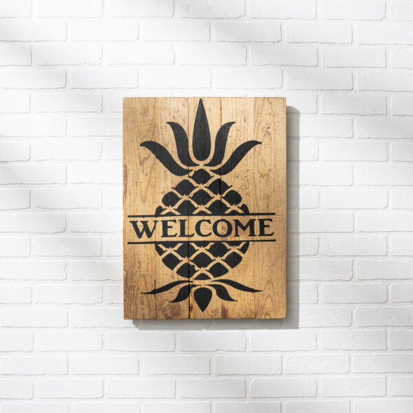 The 18x24 Welcome Pineapple sign, featuring a black pineapple design and the word "WELCOME," hangs on a white brick wall. - Spruced Studio Upscale Workshop