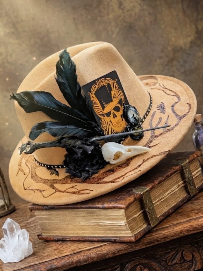 Tan hat with black feathers, a bird skull, and a skull illustration rests on an old book, with crystals nearby and a brown, vintage background. - Spruced Studio Upscale Workshop