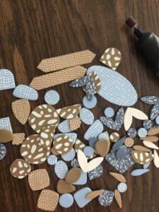Various blue, beige, and brown polymer clay pieces with different patterns are spread on a wooden surface next to a rotary tool. - Spruced Studio Upscale Workshop