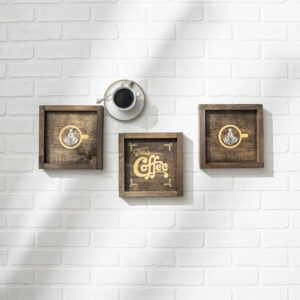 A cup of black coffee sits on a white brick wall beside three 9x9 Drink Coffee - props wall art pieces with coffee-themed designs and the words "Drink Coffee. - Spruced Studio Upscale Workshop