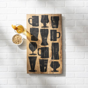 The 14x24 Beer Glasses - props 2 features a wooden board with black drinkware silhouettes, displayed beside a glass of orange drink and a bowl of peanuts on a white brick surface. - Spruced Studio Upscale Workshop