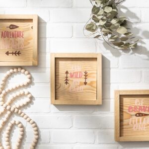Three 9x9 wooden-framed signs—Run Wild, Adventure, and Be Brave—hang on a white brick wall beside a beaded garland and dried foliage. - Spruced Studio Upscale Workshop