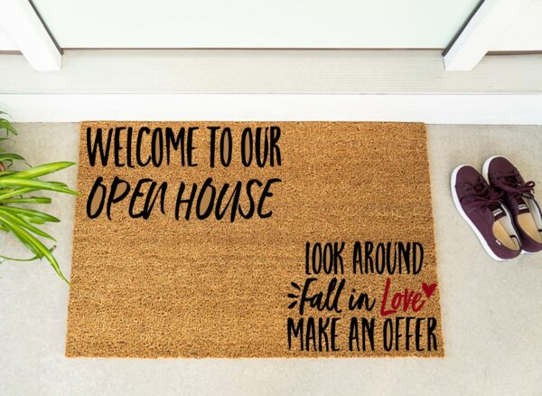 The "Welcome to Our Open House" doormat displays inviting messages and is shown next to maroon shoes and a plant by the door. - Spruced Studio Upscale Workshop