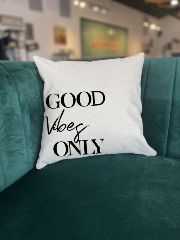 A "Good Vibes Only" white pillow rests on a green velvet couch in a modern living room. - Spruced Studio Upscale Workshop