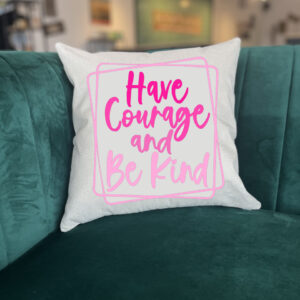 The "Have Courage Be Kind" white throw pillow with pink text rests on a green velvet couch in a modern room. - Spruced Studio Upscale Workshop