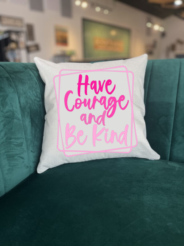 The "Have Courage Be Kind" white throw pillow with pink text rests on a green velvet couch in a modern room. - Spruced Studio Upscale Workshop