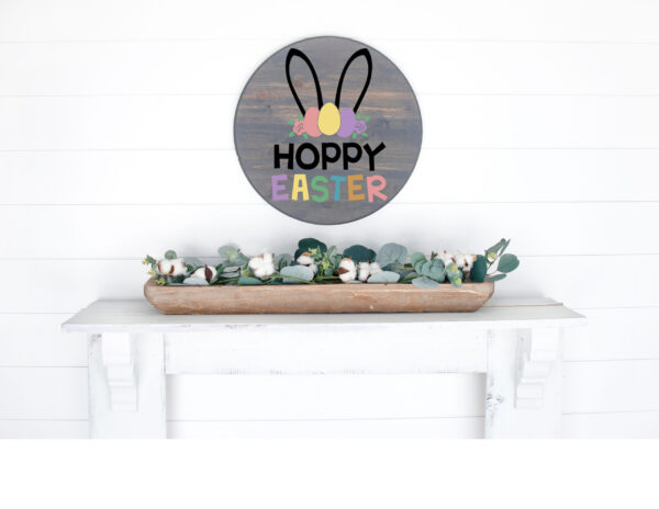 A round "Hoppy Easter" sign with bunny ears hangs above a white mantle, decorated with a wooden tray holding cotton stems and greenery. - Spruced Studio Upscale Workshop