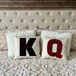 The King + Queen set features two decorative pillows on a beige bed—one with "King of his" and a bold "K," the other with "Queen of his" and a large "Q. - Spruced Studio Upscale Workshop
