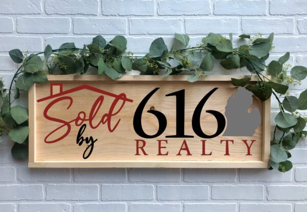 A 12x32 "Sold By 616" wooden sign with greenery features a house roof graphic and Michigan state outline, displayed against a white brick wall. - Spruced Studio Upscale Workshop