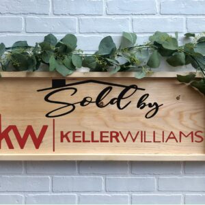 A 12x32 "Sold By Keller Williams" wooden sign with greenery is displayed against a white brick wall background. - Spruced Studio Upscale Workshop