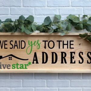 The 12x32 Said Yes to the Address - FiveStar wooden sign with greenery reads "We said yes to the address five star*" and is displayed against a white brick wall background. - Spruced Studio Upscale Workshop