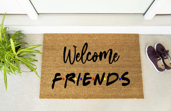 The "Welcome Friends" doormat is placed in front of a door, beside a green plant and maroon shoes. - Spruced Studio Upscale Workshop