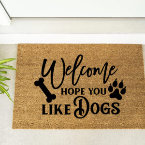 The Welcome Hope You Like Dogs doormat sits beside a plant and maroon shoes on a light-colored floor. - Spruced Studio Upscale Workshop
