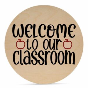 Round wooden "Welcome to Our Classroom" sign featuring two red apple icons as the letter "o" in "to" and "classroom. - Spruced Studio Upscale Workshop