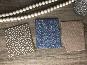 Three patterned paper envelopes in brown and blue tones are placed on a wooden surface, with a beaded garland and a decorative candle nearby. - Spruced Studio Upscale Workshop