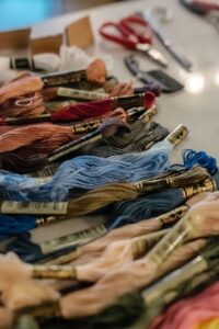 Bundles of embroidery floss in various colors are spread out on a table, with scissors and other craft tools in the background. - Spruced Studio Upscale Workshop
