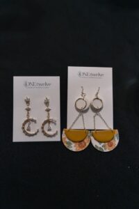 Two pairs of earrings displayed on branded cards: one pair features crescent moons with star details, the other pair has yellow semicircles with floral patterns and gold hoops. - Spruced Studio Upscale Workshop