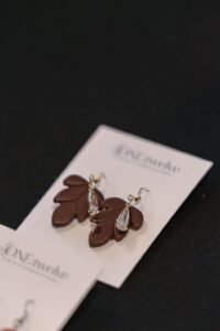 A pair of brown leaf-shaped earrings with teardrop-shaped crystal accents displayed on a branded card against a black background. - Spruced Studio Upscale Workshop
