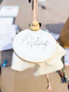 A wooden embroidery hoop holds fabric with a simple stitched design of flowers and stems, resting on a table with sewing materials nearby. - Spruced Studio Upscale Workshop