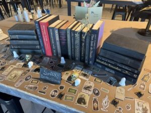 A row of vintage books stands on a decorated table covered with Halloween-themed stickers, small skulls, and ghost figurines. - Spruced Studio Upscale Workshop