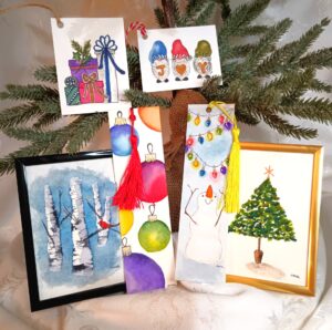 Assorted watercolor holiday-themed cards, bookmarks, and framed art featuring a snowman, a Christmas tree, ornaments, birch trees, and the word "JOY" displayed in front of pine branches. - Spruced Studio Upscale Workshop