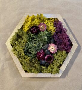 A hexagonal wooden frame filled with green, yellow, and purple preserved moss and dried flowers, arranged decoratively on a brown surface. - Spruced Studio Upscale Workshop