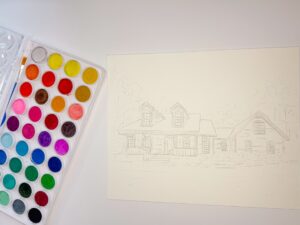 A watercolor paint palette sits next to a sheet of paper with a lightly sketched outline of a house and trees. - Spruced Studio Upscale Workshop