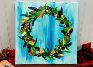 A colorful, hand-painted wreath with green leaves and red, purple, and yellow accents on a light blue canvas background. - Spruced Studio Upscale Workshop