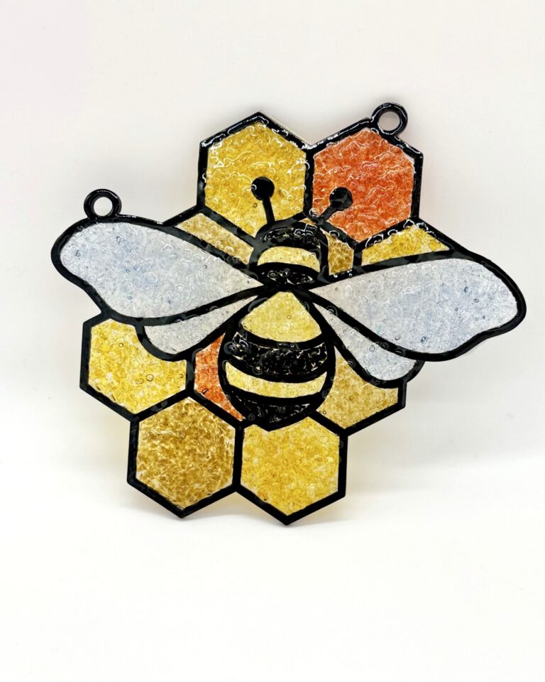 Stained glass ornament depicting a bee with outstretched wings on a honeycomb background in shades of yellow and orange. - Spruced Studio Upscale Workshop