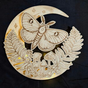 A wooden cutout featuring a moth on a crescent moon, surrounded by ferns, mushrooms, and small stars, set against a dark background. - Spruced Studio Upscale Workshop