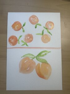 A sheet of paper with watercolor paintings of oranges and green leaves, arranged in two groups separated by a horizontal line, on a wooden surface. - Spruced Studio Upscale Workshop